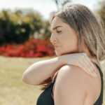 Woman in black tank top touching shoulder outdoors. Concept of shoulder pain and relaxation.