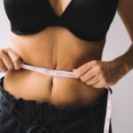 A woman measures her waist with a tape for fitness and weight loss results.