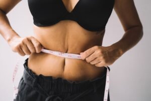 A woman measures her waist with a tape for fitness and weight loss results.