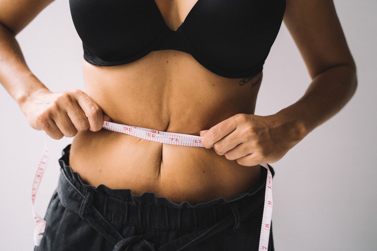A woman measures her waist with a tape for fitness and weight loss results.